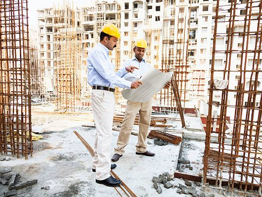 engineer and architect discussing blueprint on construction site in India