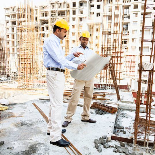 engineer and architect discussing blueprint on construction site in India